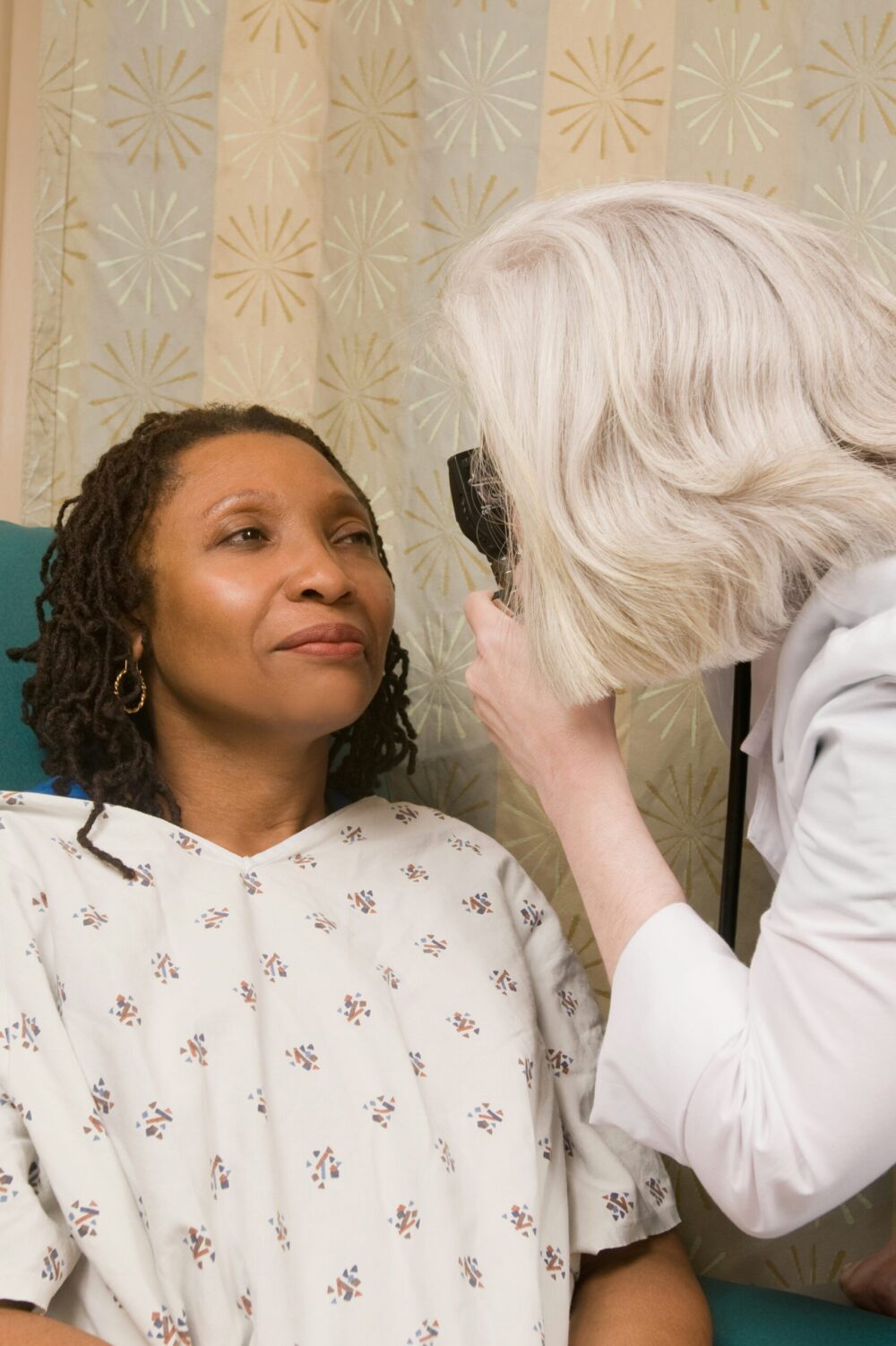 White female doctor using an ophthalmoscope to examine the eyes of her Black female patient