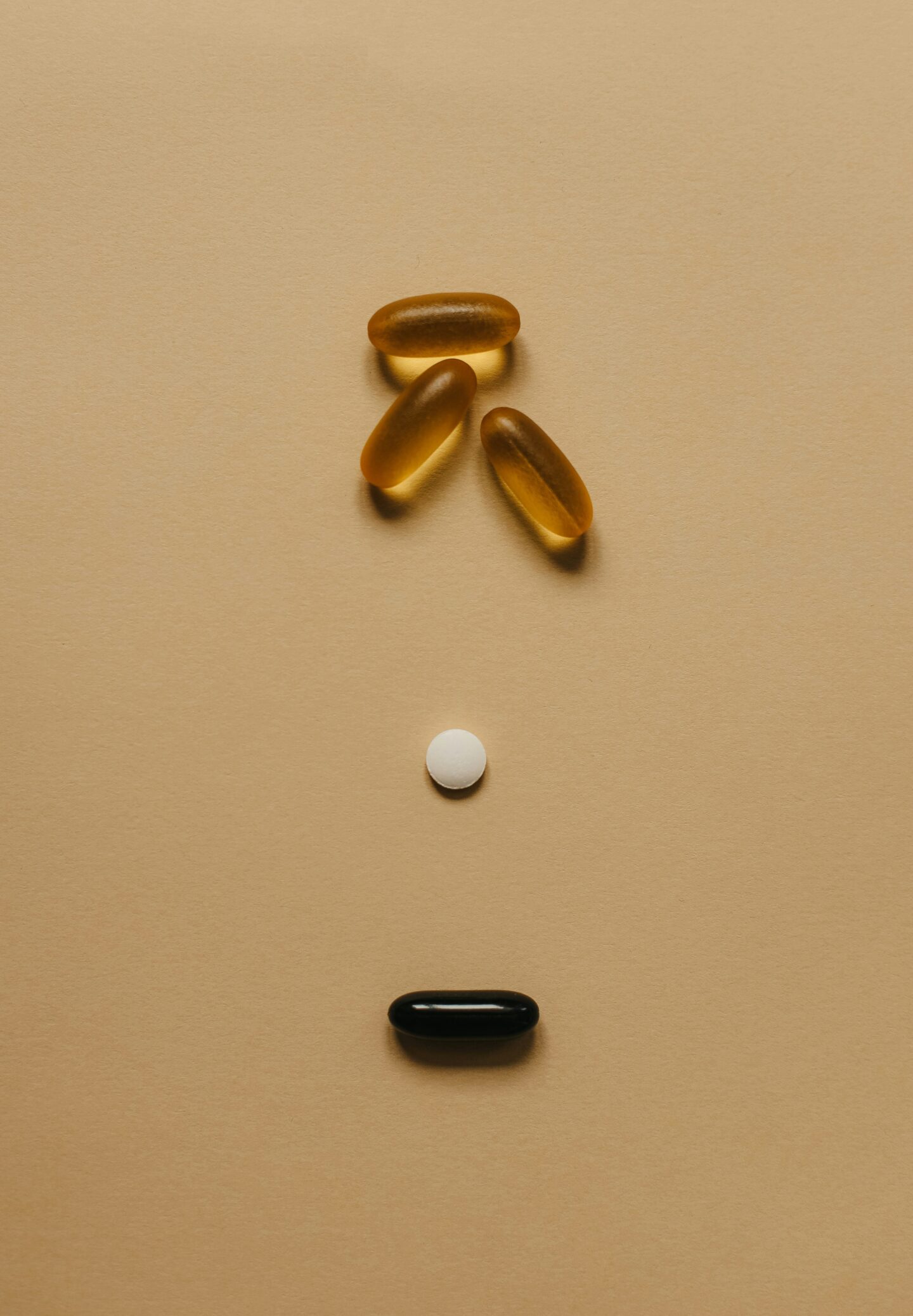 Three fish oil capsules, a white pill, and a black pill placed on brown paper